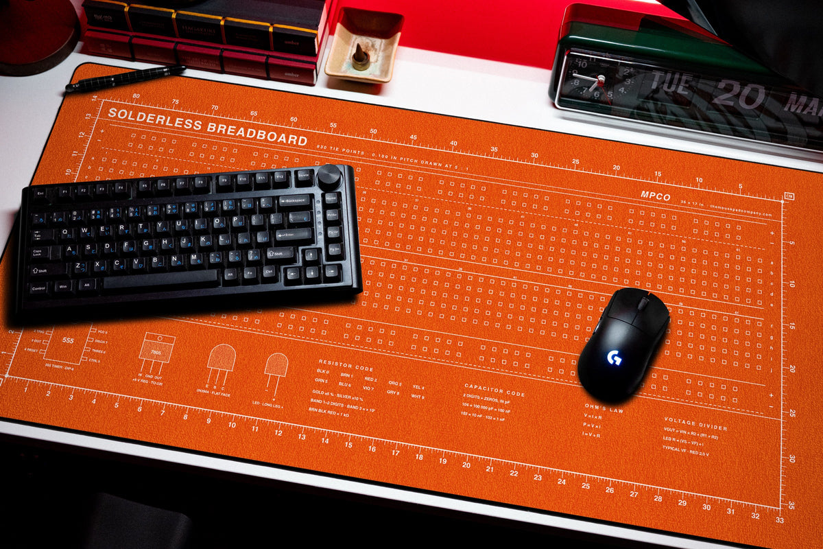 Breadboard Pad desk mat in Orange / White, shown on a styled desk setup