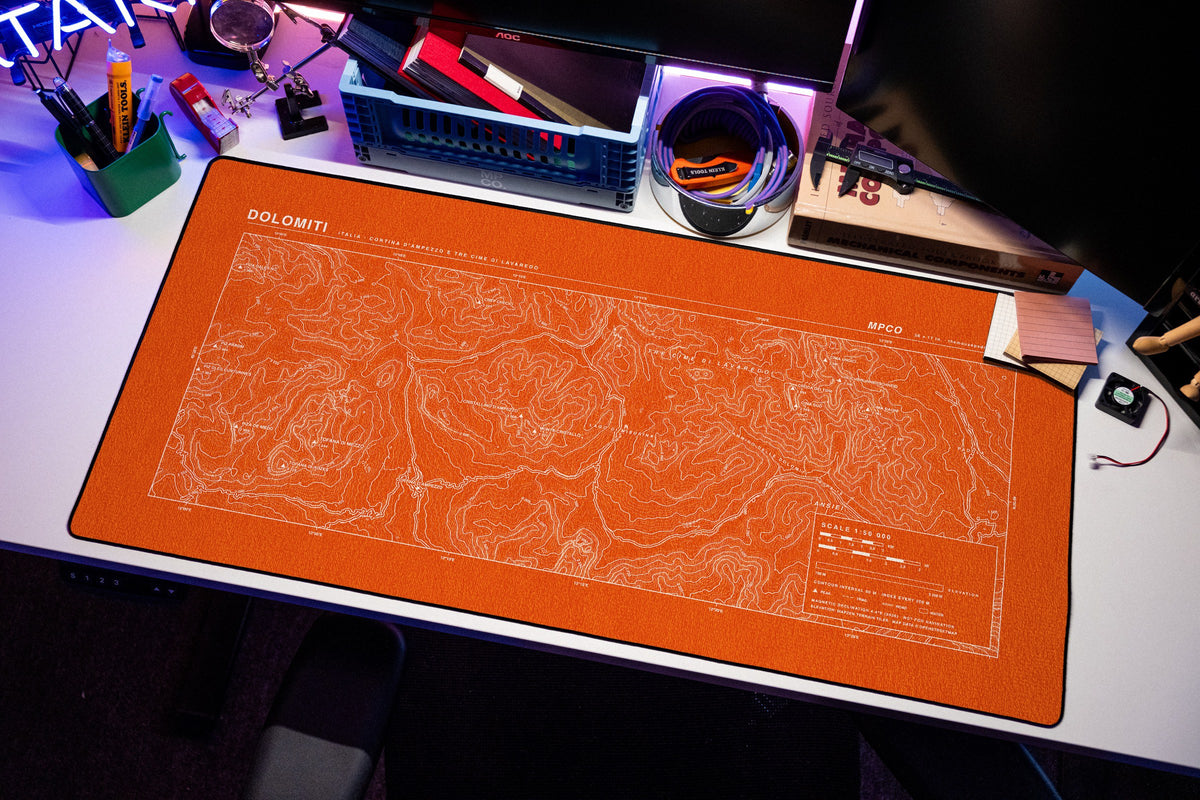 Dolomites Topo Pad desk mat in Orange / White, shown on a styled desk setup