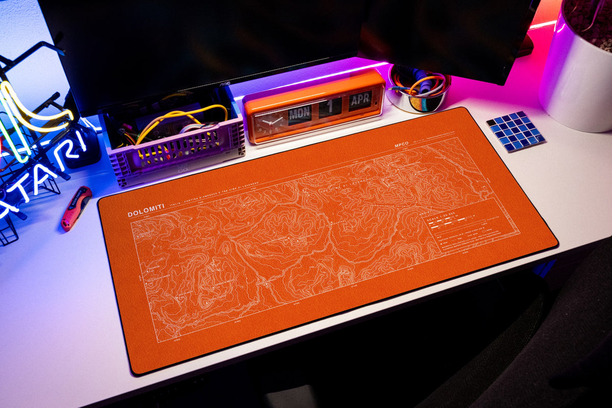 Dolomites Topo Pad desk mat in Orange / White, shown on a styled desk setup