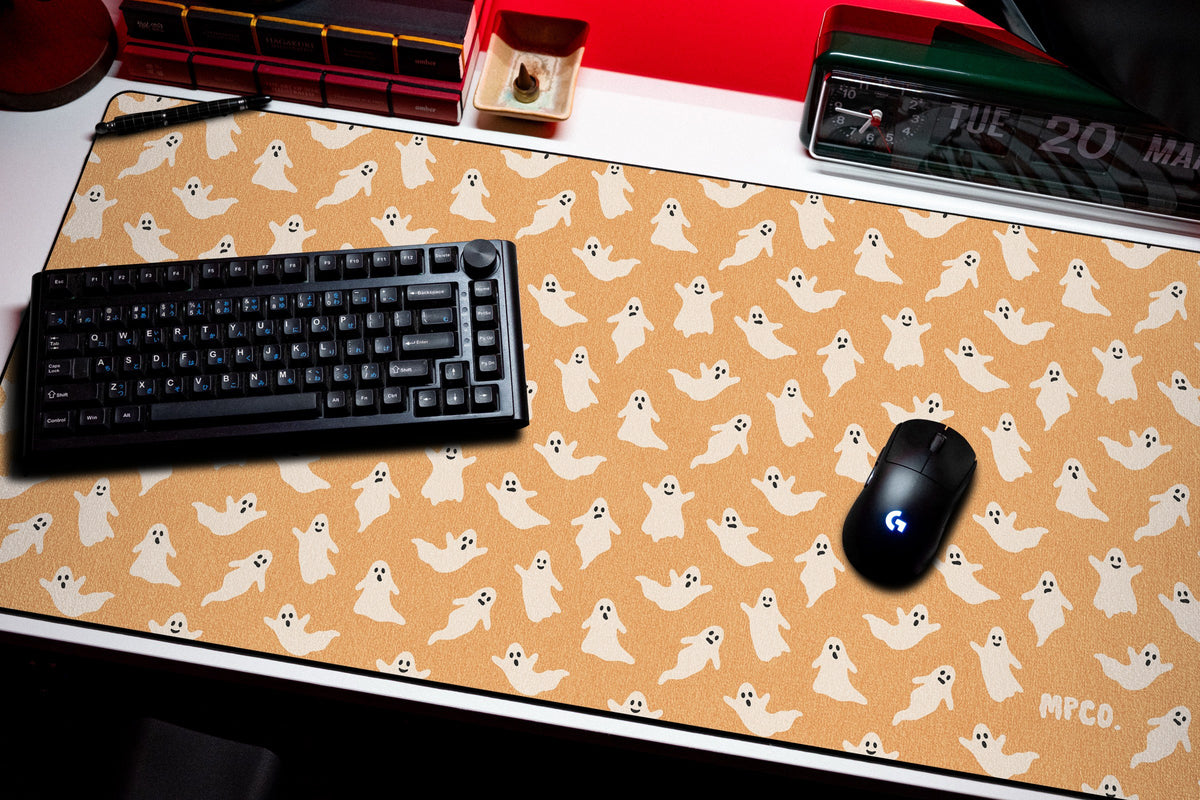 Ghosts desk mat in Orange, shown on a styled desk setup