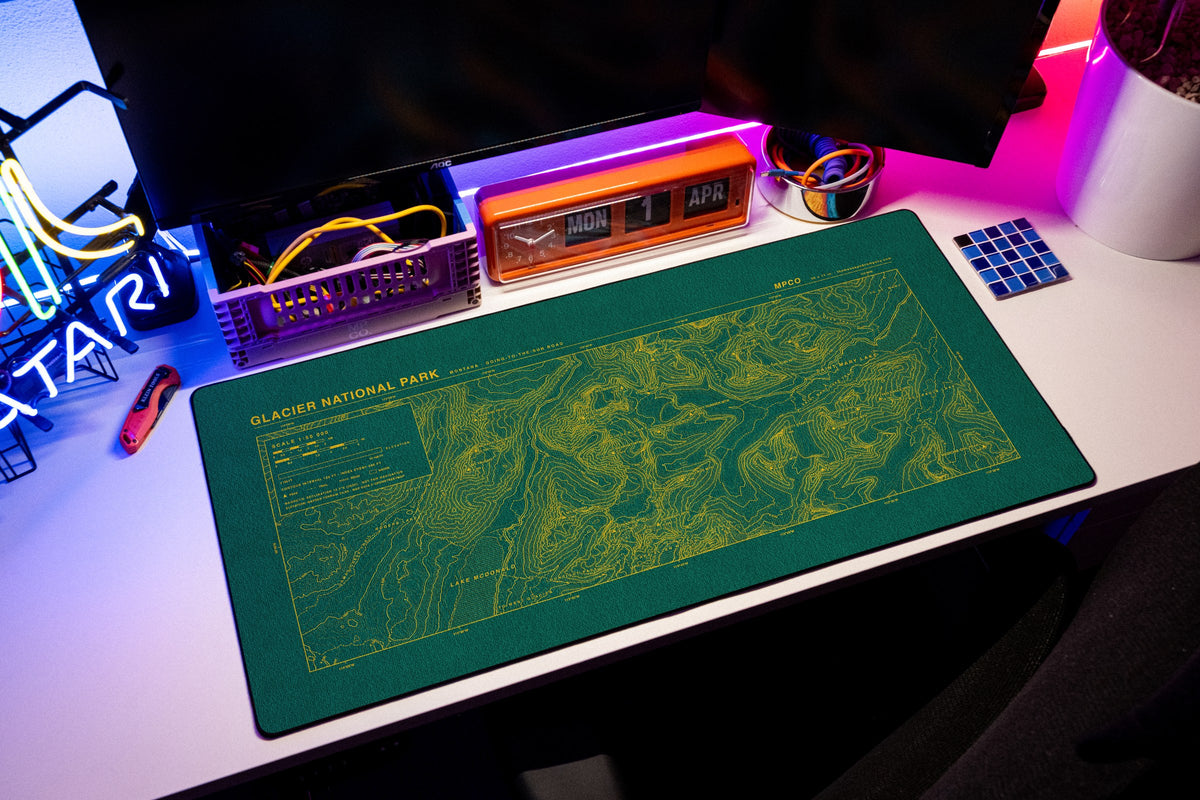 Glacier National Park Topo Pad desk mat in Green / Yellow, shown on a styled desk setup
