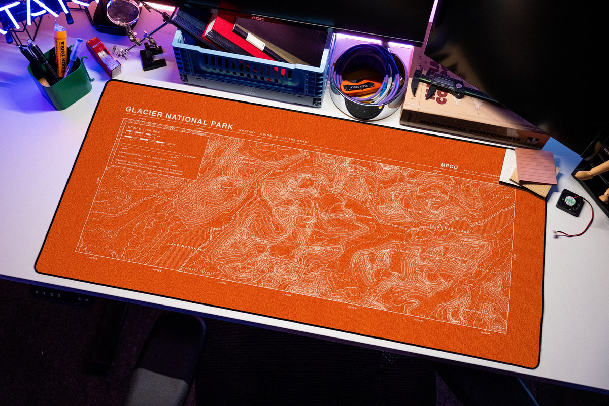Glacier National Park Topo Pad desk mat in Orange / White, shown on a styled desk setup