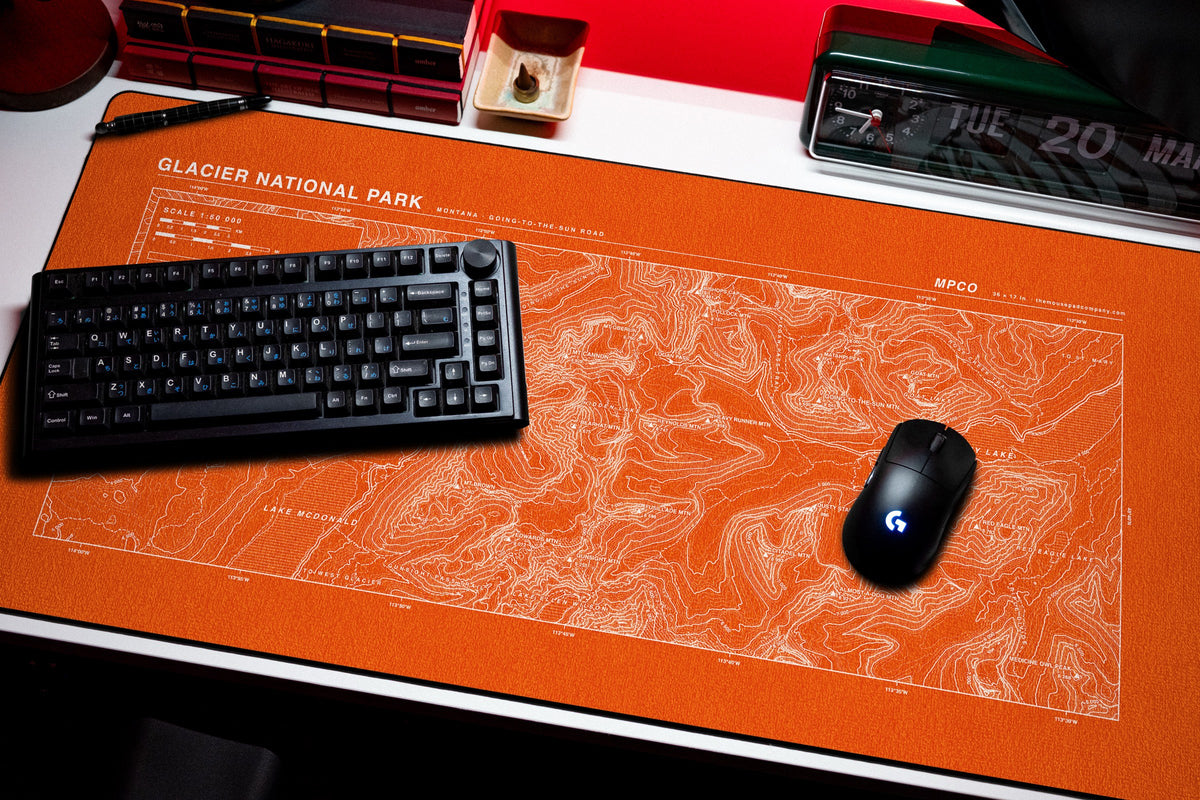 Glacier National Park Topo Pad desk mat in Orange / White, shown on a styled desk setup