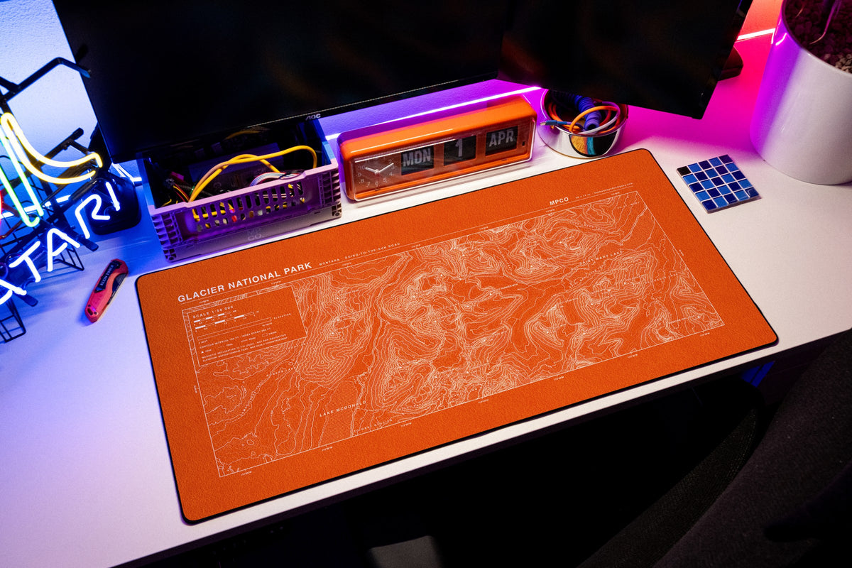 Glacier National Park Topo Pad desk mat in Orange / White, shown on a styled desk setup
