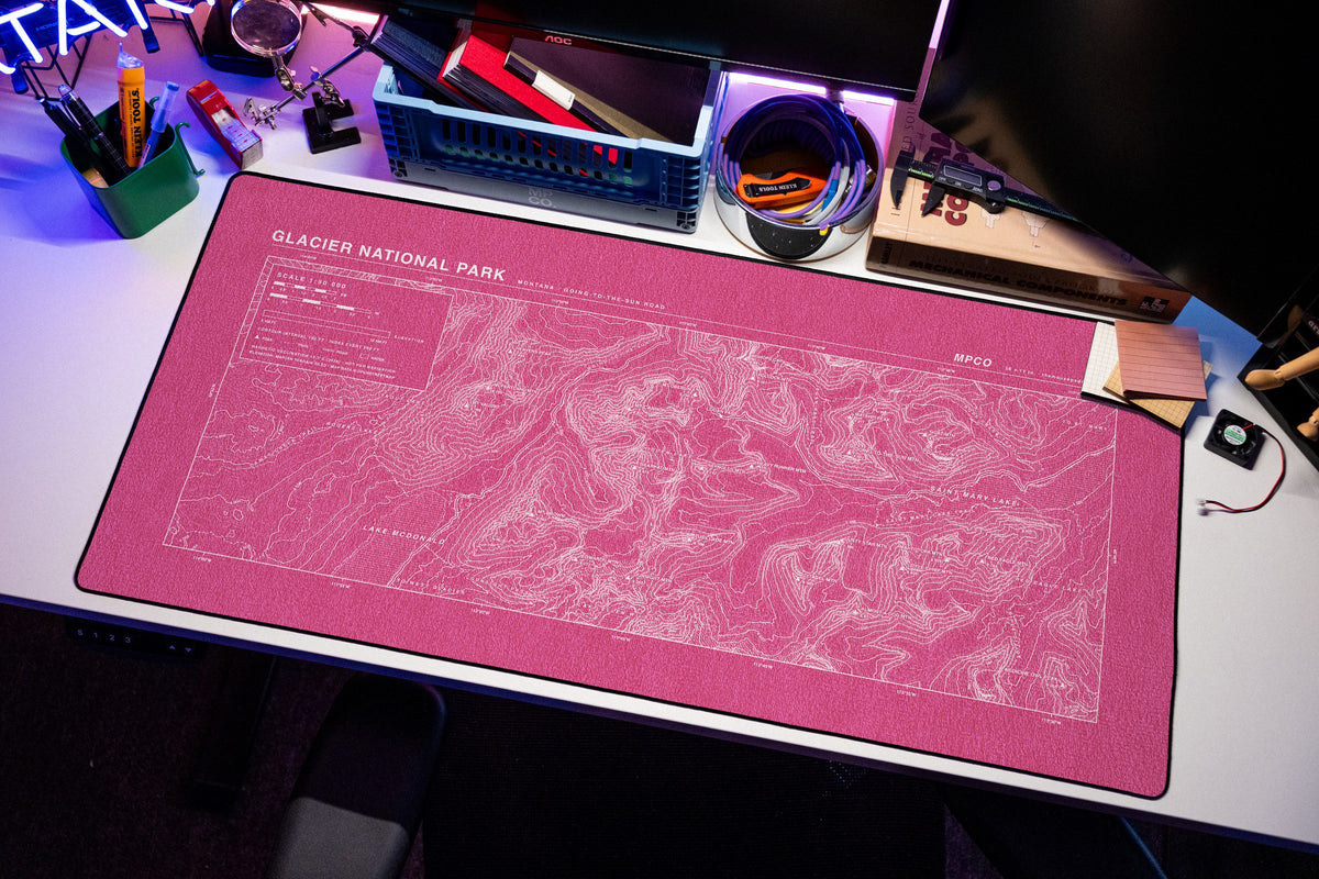 Glacier National Park Topo Pad desk mat in Pink / White, shown on a styled desk setup