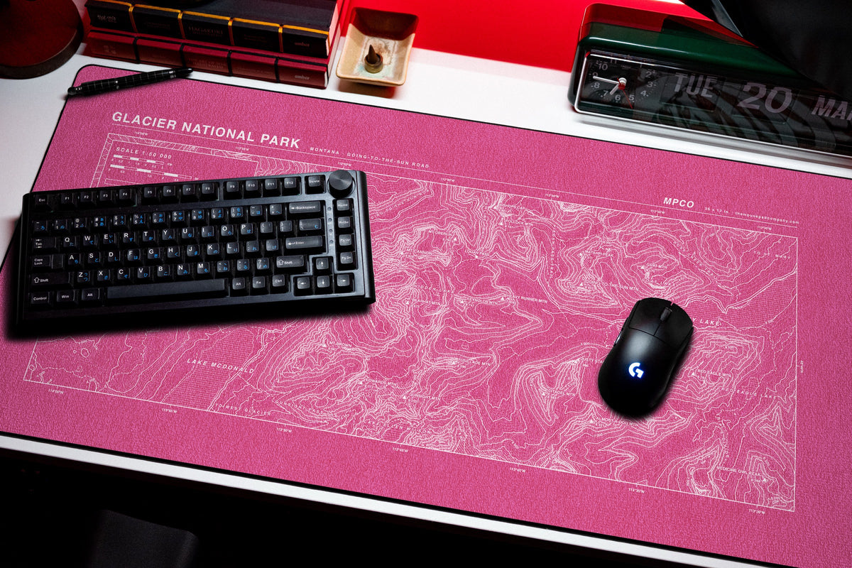 Glacier National Park Topo Pad desk mat in Pink / White, shown on a styled desk setup