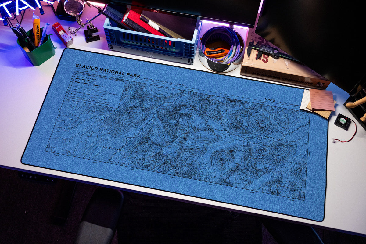 Glacier National Park Topo Pad desk mat in Swiss Blue, shown on a styled desk setup