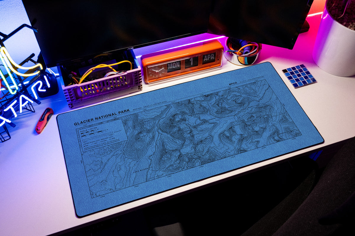 Glacier National Park Topo Pad desk mat in Swiss Blue, shown on a styled desk setup