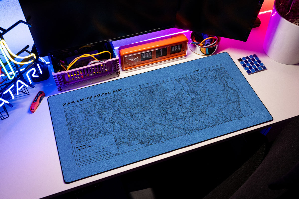 Grand Canyon National Park Topo Pad desk mat in Swiss Blue, shown on a styled desk setup