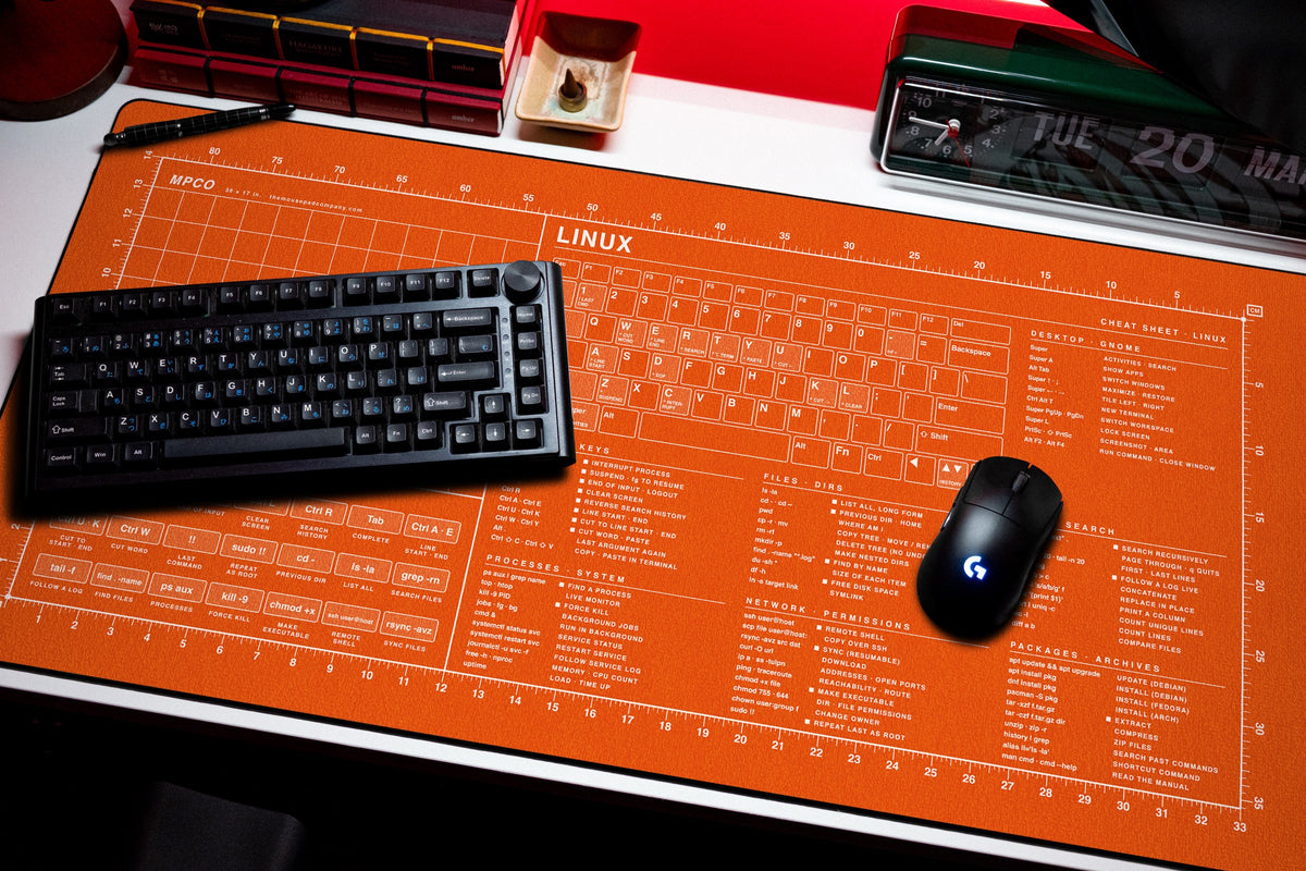 Linux Cheat Sheet Pad desk mat in Orange / White, shown on a styled desk setup