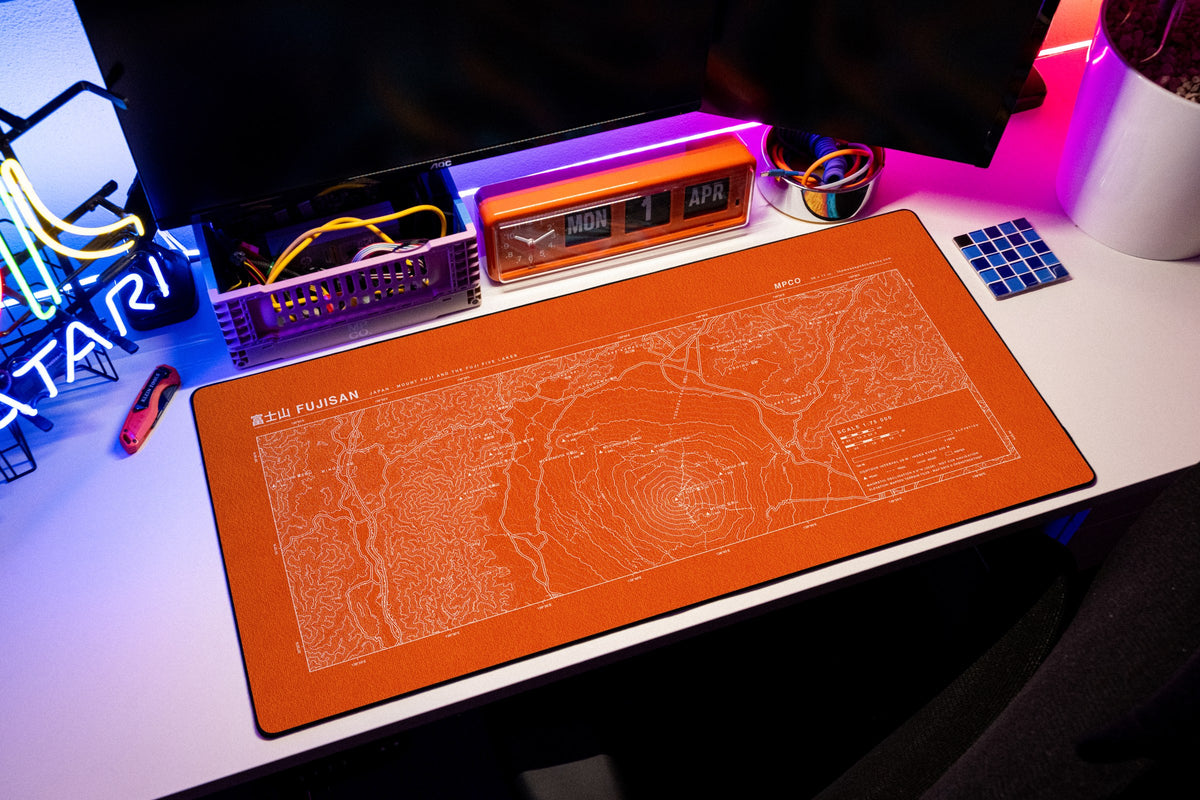 Mount Fuji Topo Pad desk mat in Orange / White, shown on a styled desk setup